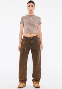 Bruin gestreept cropped t-shirt met logo, gecombineerd met losse bruine denim broek met accentstiksels en gouden hardwaredetails.