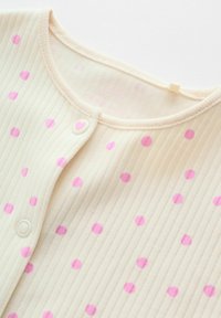 Tissu côtelé crème avec des pois roses, col rond et bouton pression orné d'un petit cœur rose.