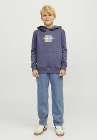 Paarse hoodie met een voorzak, featuring het "JACK & JONES" logo. Gepaard met lichtblauwe jeans en sneakers met groene en witte strepen.