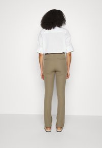 Calças flare de cintura alta bege, com um tecido suave, dois bolsos traseiros e um corte ajustado, combinadas com uma camisa branca de mangas curtas.