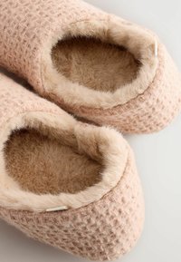 Rosa gewebte Hausschuhe mit einer strukturierten Oberfläche, die ein weiches, fellartiges Futter aufweisen. Das Design ist einfach mit einer abgerundeten Öffnung und neutralen Akzenten.