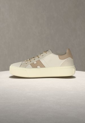 Beiger und weißer Sneaker mit niedrigem Schaft, Schnürverschluss, beigefarbenem Fersenlaschen und beiger Seitenstreifen auf off-weißer Gummisohle.