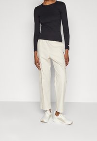 Černý dlouhý rukáv, béžové cargo kalhoty s elastickým pasem a bílé tenisky s béžovými akcenty. Hladká látka, volný střih.