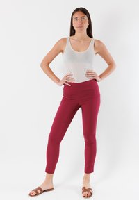 Pantaloni marsala aderenti con vita alta, texture morbida e design senza cuciture. Indossati con un top grigio chiaro e sandali marroni.