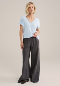 Gai zils V-veida krekls ar strukturētu zigzaga rakstu, saskaņots ar platām melnām biksēm ar gludu audumu.