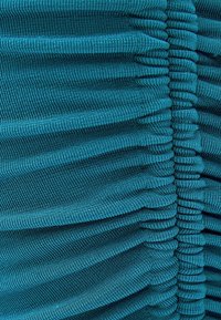 Tissu en maille ribbed teal présentant des détails de ruching verticaux, créant profondeur et texture. Surface lisse avec une couleur et un motif uniformes.
