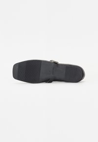 Semelle d'une chaussure plate noire à bout carré avec une semelle texturée, montrant la taille et les marquages "Made in China".