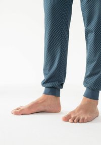 Blauwe joggingbroeken met een patroon van kleine witte stippen, elastische boorden en een gladde textuur. Blote voeten zichtbaar onderaan.