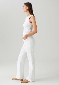 Top aderente bianco abbinato a pantaloni bianchi svasati, che mostra un tessuto morbido e un design pulito. Il look è completato da scarpe beige.