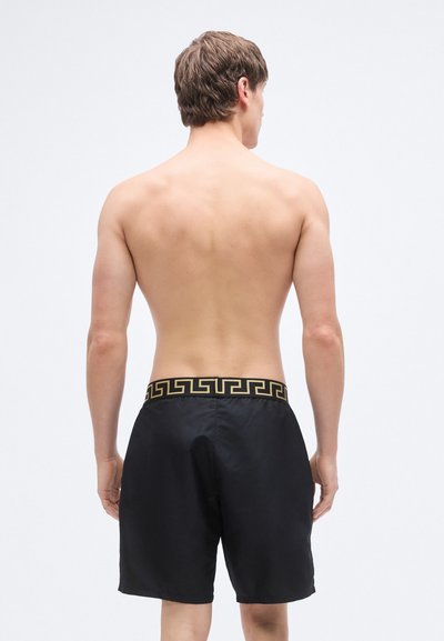 Zwarte zwembroek met een gouden Griekse sleutelmotief op de tailleband, gemaakt van lichtgewicht, glad materiaal, met een losse pasvorm.