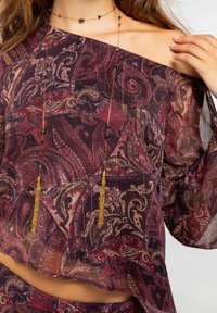 Top transparente, con los hombros al descubierto y un patrón de paisley en tonos de burdeos y dorado. Acentuado con un largo collar de cuentas con cuentas rojas y negras.