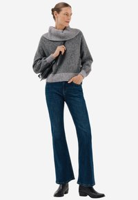 Szary dzianinowy sweter z szerokim, prążkowanym kołnierzem; zestawiony z ciemnoniebieskimi spodniami dzwonami i czarnymi botkami za kostkę. Prosty design, miękka faktura.