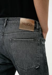 Černé džíny z denimu s jemnou strukturou, kožený štítek s nápisem "HUGO" a klasickým detaily na zadních kapsách.