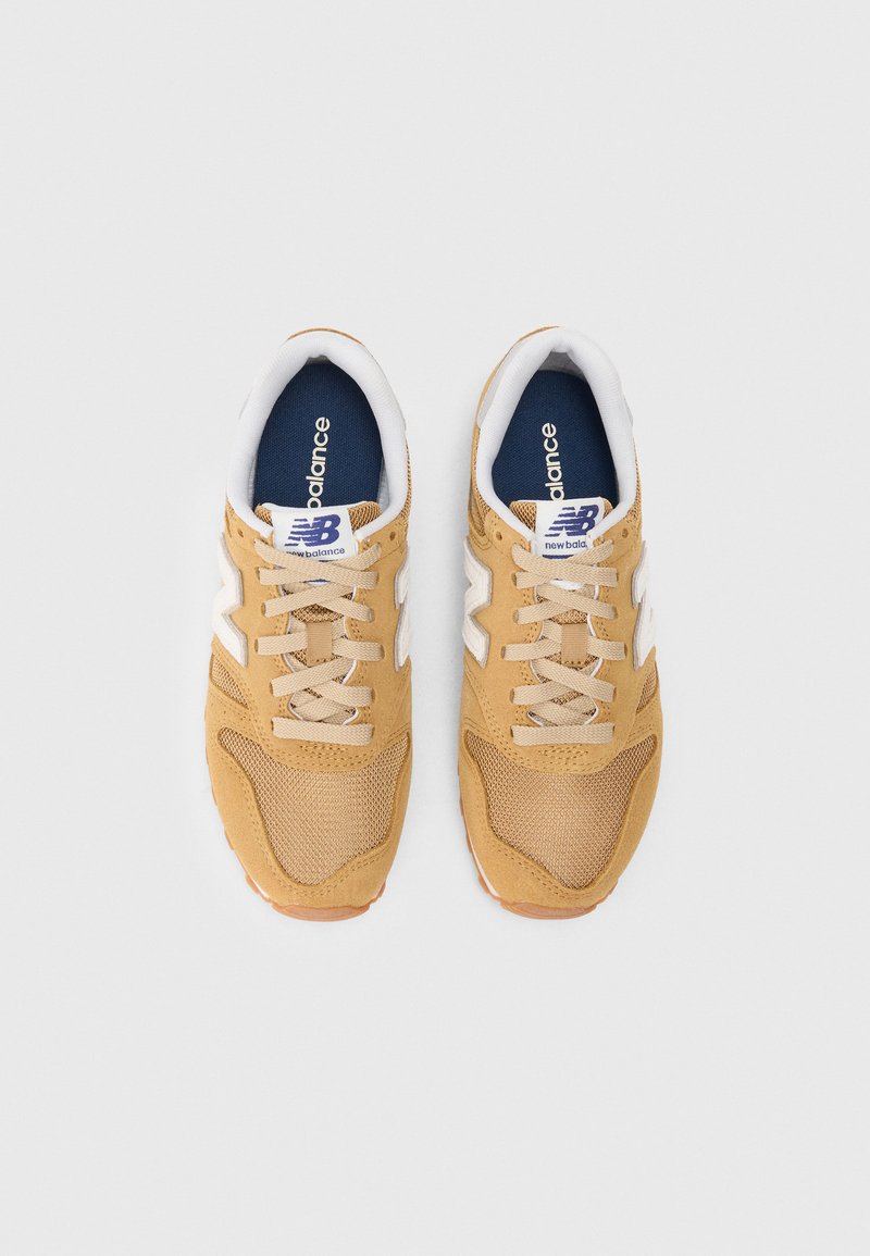 Baskets beiges en maille et daim, avec des accents blancs, des lacets beiges et une semelle intérieure marine arborant le logo New Balance.