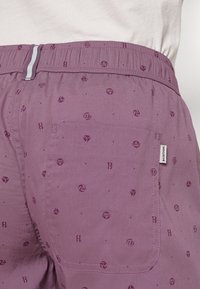 Purple shorts with a lightweight fabric, featuring a subtle pattern of logos and numbers, elastic waistband, and a back pocket.