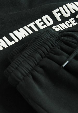 Czarny bawełniany sweatshirt z białym napisem "NIEOGRANICZONE ŚRODKI OD" oraz pasującymi czarnymi dresami z elastycznym paskiem i sznurkiem.