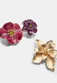 Tre blomsterbrocher: en dyb pink emalje blomst, en lilla harpiksblomst med perler, og en blomster i guldfarvet metal med teksturerede kronblade.