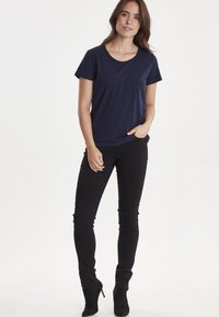 Navy blå kortærmet t-shirt lavet af blødt stof, parret med sorte tætsiddende jeans og sorte ankelstøvler. Simpelt design, ingen mønstre.