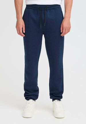 Navy blauwe sweatpants met een trekkoord in de taille, taps toelopende benen en een zachte textuur. Gekocht met witte sneakers voor contrast.
