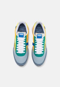 Mehrfarbige Sneaker aus einer Kombination von grauem, grünem, gelbem und blauem Material, mit weißen Schnürsenkeln und einem Logopatch auf der Zunge.