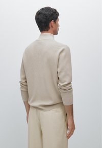 Beige ribbed knit sweater with a collar, long sleeves, and fitted cuffs, paired with beige trousers. Subtle texture, minimalist design.