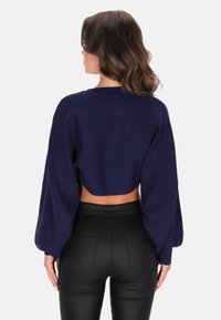 Pulover scurt de culoare bleu marin cu textură ribbed, mâneci ballooney și decolteu larg, asortat cu pantaloni negri cu talie înaltă.