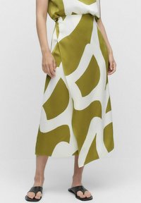 Olijfgroene en witte gestreepte rok met een asymmetrische onderrand, gemaakt van een gladde stof. G gedragen met zwarte sliding sandalen.