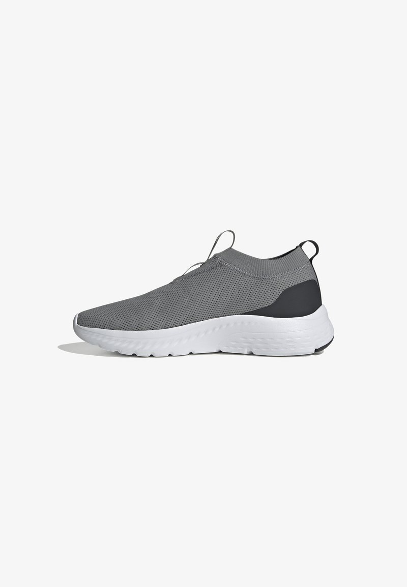 Chaussure de sport grise en maille avec un design sans lacets, semelle blanche et un accent noir au talon. Présente une surface texturée et une languette de traction.