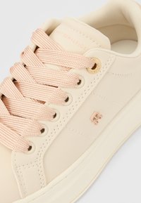 Bež superga s gladkim usnjenim zgornjim delom, svetlo roza vezalkami, zlato barvnimi ojalami in vtisnjenim logotipom na strani. Zaobljen prst in eleganten dizajn.