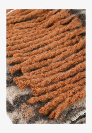 Manta texturizada con flecos anaranjados retorcidos y suaves. La base tiene tonos gris y crema con acentos negros. El material parece cálido y esponjoso.