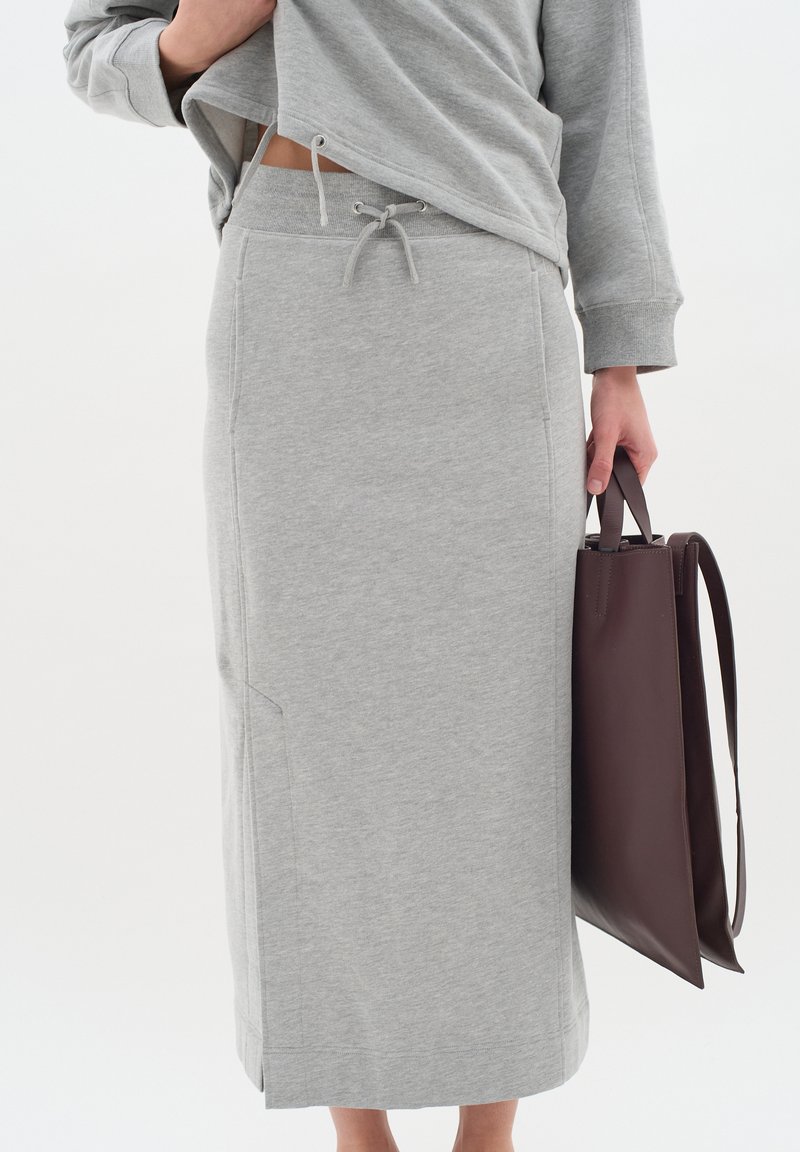 Grijze, knie-lange rok van zacht materiaal met een elastische tailleband en een trekkoord, gecombineerd met een donkerbruin leren handtas.