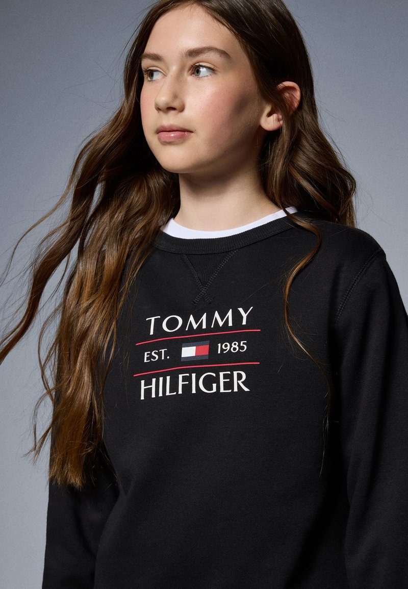 Fekete pulóver "TOMMY HILFIGER" logóval fehér és piros színben, kerek nyakkal, texturált anyagból k�észült, és látható varrási részletekkel.