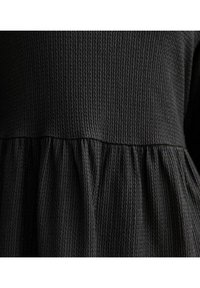 Top negro de tela texturizada con cinturilla fruncida, con un patrón acanalado distintivo y una costura suave que divide el busto de la falda.