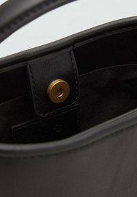 Interno della borsa a tracolla in pelle nera caratterizzato da una chiusura a scatto con bottone dorato e un rivestimento leggermente testurizzato. Marchio visibile su un'etichetta interna.