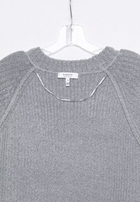 Pull en tricot gris avec une texture côtelée, doté d'un col rond et de manches raglan. L'étiquette indique le nom de la marque et la taille S.