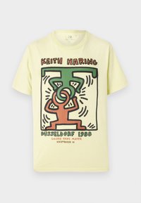 Yellow cotton T-shirt featuring a graphic print of intertwined figures in red and green, with "Keith Haring DÜSSELDORF 1988" text below.