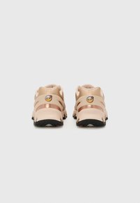 Beige sportieve schoenen met een gestructureerd oppervlak, uitsnijdingen in het ontwerp en zwarte rubberen zolen. Beschikt over een klein logo op de hiel.