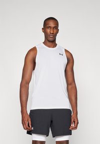 Débardeur de sport sans manches blanc avec un col rond et un petit logo noir sur la poitrine, associé à un short foncé.