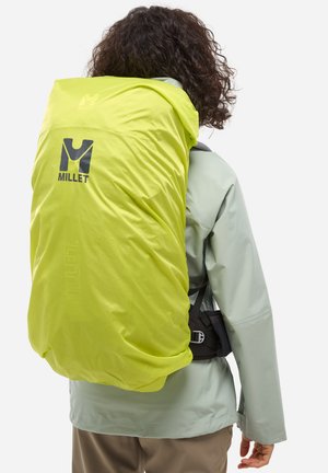 Sac à dos jaune vif Millet avec une finition résistant à l'eau, harnais noir ajustable et détail de logo. Porté par-dessus une veste gris clair.