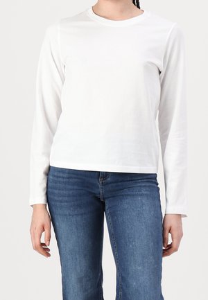 Person wearing a plain white long-sleeve shirt and blue denim jeans, standing against a neutral background.