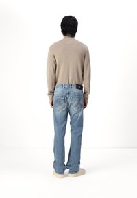 Lichtbruine trui met een hoge hals, gecombineerd met een medium gewassen, relaxed-fit jeans. Kenmerkende stiksels op de achterzak, crèmekleurige sneakers.