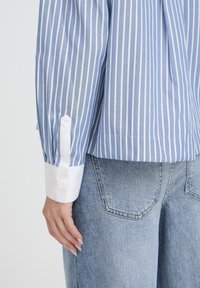 Blauw-wit gestreepte blouse met een witte manchet en knoopsluiting, gecombineerd met lichtblauwe denim broek met een klassiek zakontwerp.