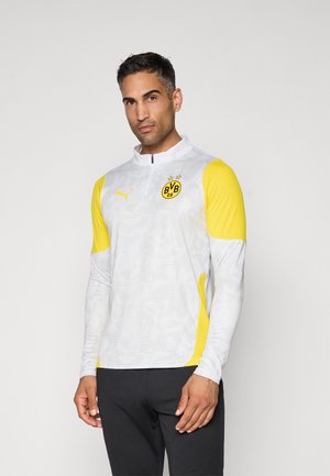 Langærmet sportstop i hvid og gul med lynlås i nakken, logo på brystet og struktureret design på ærmerne og torso.