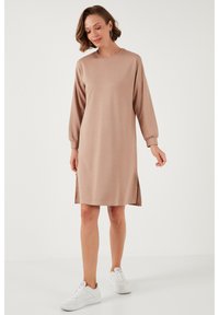 Beige sweatshirt dress with long sleeves, round neckline, side slits, and a relaxed fit, paired with white sneakers. Smooth texture.