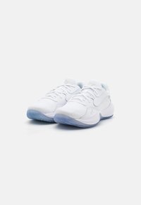 Baskets blanches de sport avec un tissu texturé, un design à lacets et une semelle translucide bleu clair. Présente un logo discret sur le côté.