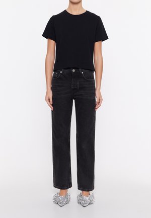 Black cropped t-shirt with short sleeves, paired with high-waisted black jeans. Footwear features silver ruffled accents on pointed heels.