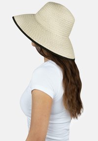 Breiter Strohhut in natürlicher Farbe mit schwarz-weißem Rand, rundem Kopf und strukturiertem Webdesign, aus einer Perspektive präsentiert.