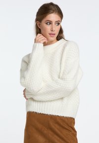 Krém színű, oversized pulóver, texturált mint�ával, bordázott mandzsettákkal és szegéllyel. Barna velúr szoknyával viselve. Egyszerű, letisztult dizájn.