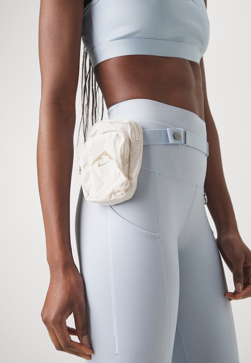 Leggings de sport bleu clair associés à une pochette beige. La pochette est dotée d'une fermeture éclair et d'un logo doré. L'ensemble est complété par un crop top assorti.