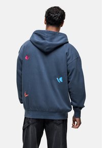 Navy blue hoodie made of soft fabric, featuring colorful butterfly prints in pink and blue on the back. Relaxed fit with a large hood.